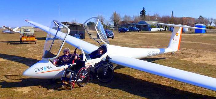 Avioneta sin motor con dos personas montadas y la silla de ruedas en el suelo